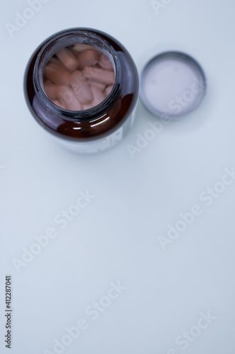 Vertical shot of an uncapped bottle of tablets on a white surface with space for your text photo