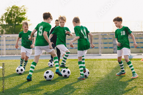 Group of children playing soccer on training session. Kids in football club wearing blue jersey shirts and soccer kits. Happy boys practicing football with coach on a sunny day
