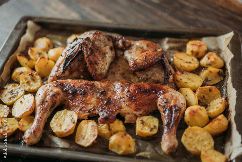 Grilled or roasted Chicken Tobacco on paper over baking sheet . Homemade freshly baked whole juicy chicken with potatoes, herbs, pepper. Selective focus, close up view. Organic country food. Grilled or roasted Chicken Tobacco on paper over baking sheet . Homemade freshly baked whole juicy chicken with potatoes, herbs, pepper. Selective focus, close up view. Organic country food.