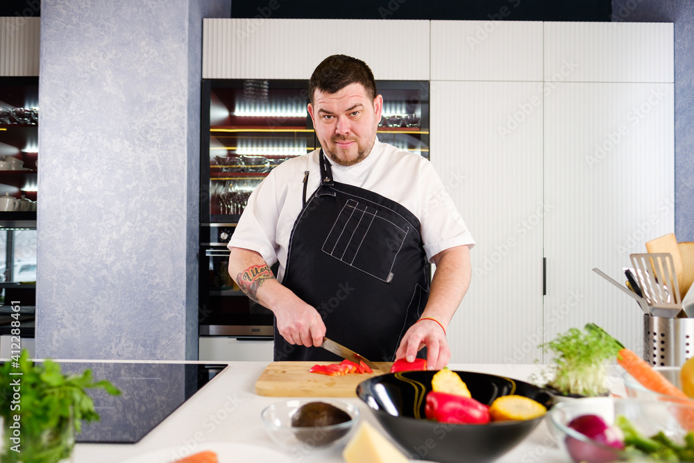 40 years man chef cooker in a white uniform and a black apron in the kitchen of the restaurant prepares a salad of vegetables and fish. 40 years man chef cooker in a white uniform and a black apron in the kitchen of the restaurant prepares a salad of vegetables and fish.
