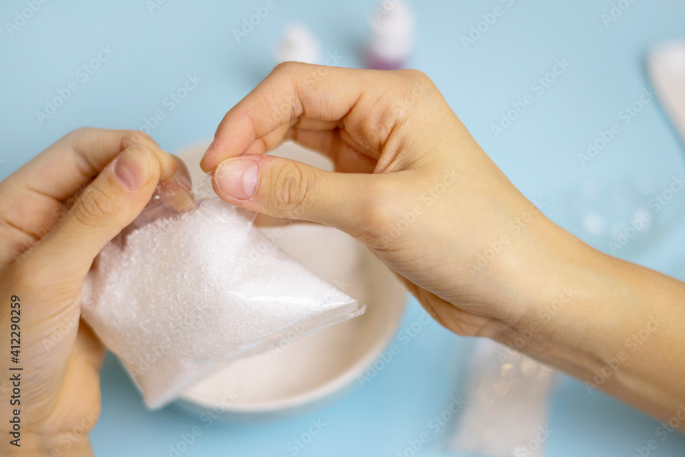 a child makes a bath bomb from sea salt, citric acid, soda, dye and flavor on a blue background, instructions, step 1 a child makes a bath bomb from sea salt, citric acid, soda, dye and flavor on a blue background, instructions, step 1