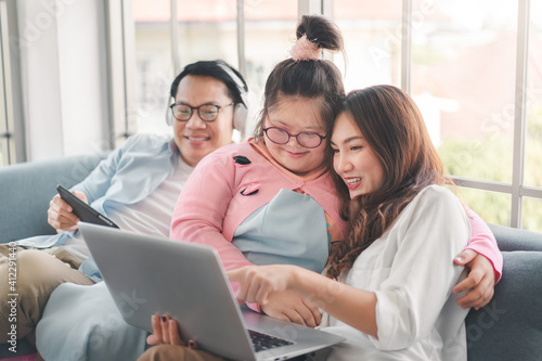 Happy asian family with their daughter down syndrome child sitting on sofa have fun using laptop watch a movie for education , Enjoy relax timing together, Activity happy family lifestyle concept.