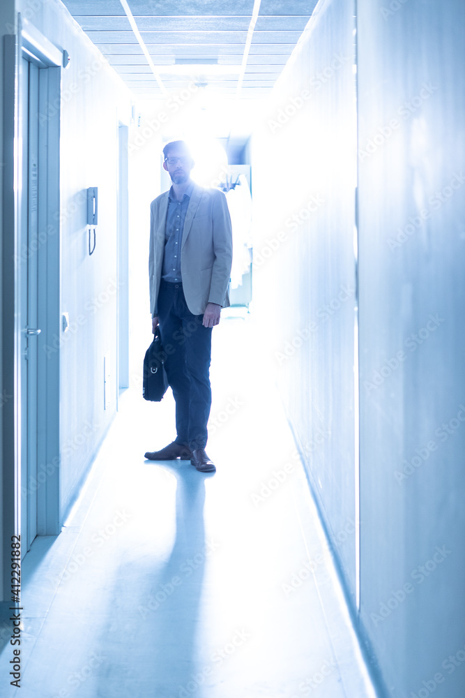 Silhouette of doctor along a hospital ward with his own briefcase, backlit lighting and cool light tone