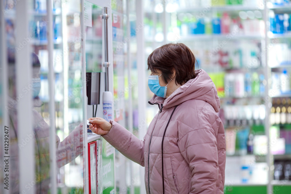 An adult woman in a medical mask buys medicine and pays at the pharmacy with a card.