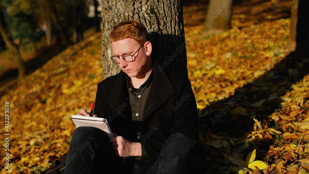 Young guy sits in an autumn park and makes notes in a notebook. Young guy sits in an autumn park and makes notes in a notebook.