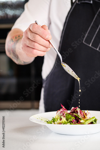 Chef finishing her plate. The cook pours the salad from a spoon with sauce.