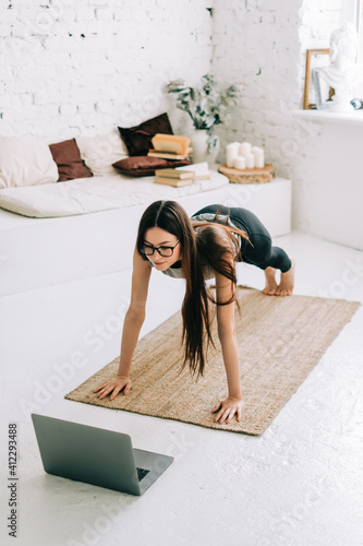 Beautiful brunette fitness woman make stretching exercises in front laptop, doing yoga indoors at home. Staying fit and healthy