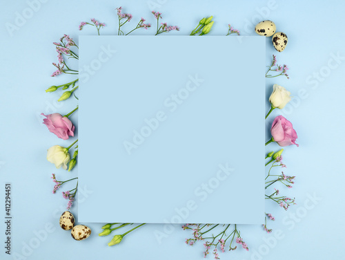 Easter composition. Easter eggs, flowers, paper blank on pastel blue background. Flat lay, top view, copy space, mock up.