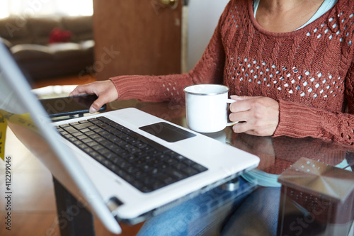 hispanic woman working from home on her laptop and drinking a cup of coffee