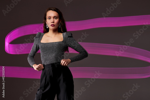 slim model against the backdrop of purple freezelight lines, attractive lady in dress posing isolated over dar studio background photo