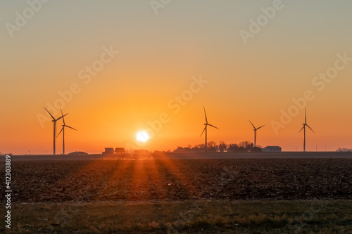 Wind turbines spin in the early morning light, with small family farms in the background. Concepts of the environment, green energy, and the Midwest