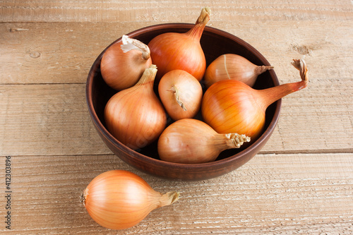 unpeeled ripe onions in a clay bowl on a light wooden background