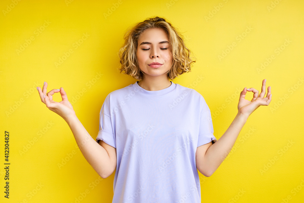 female with short hair meditating with eyes closed, isolated on yellow background. blond young caucasian woman stands in yoga pose, keeps calm female with short hair meditating with eyes closed, isolated on yellow background. blond young caucasian woman stands in yoga pose, keeps calm