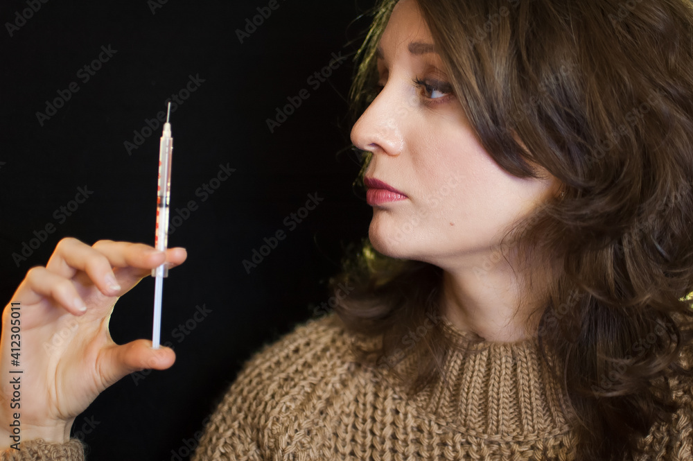 Obraz premium Vaccine concept. Female portrait of caucasian girl holding a syringe and looking at it on black background in studio.