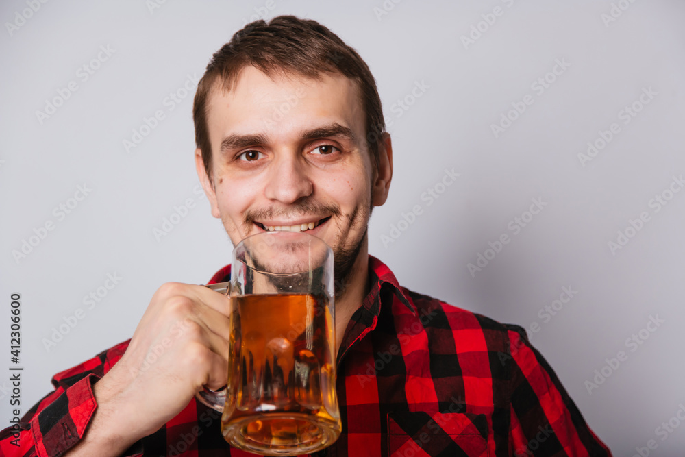 Young man in a checkered red shirt holding a large mug of beer without foam on a white background. Young man in a checkered red shirt holding a large mug of beer without foam on a white background.