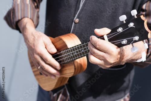 Senior person playing soprano ukulele on the street.