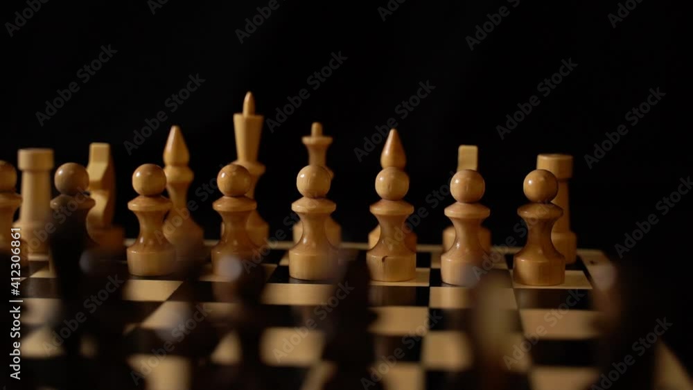 White and black wooden pieces on a chessboard. A chessboard set up during a game on a black background White and black wooden pieces on a chessboard. A chessboard set up during a game on a black background