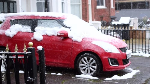 Red car parked by a house under heavy snow.