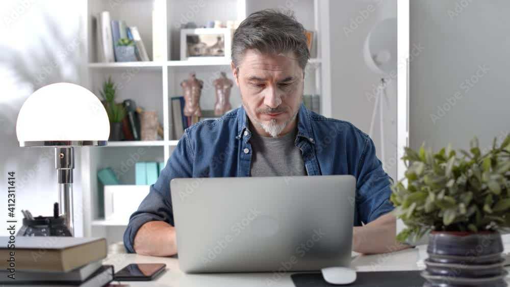Older man working online with laptop computer at home sitting at desk. Home office, browsing internet, study room. Older man working online with laptop computer at home sitting at desk. Home office, browsing internet, study room.
