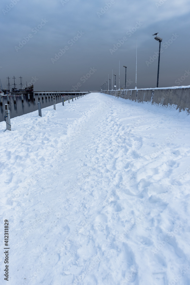 Photo of the pier at the dock. The scene takes place in winter and shows a straight, at first blurred path across the bridge. There is a blurry ship in the background.