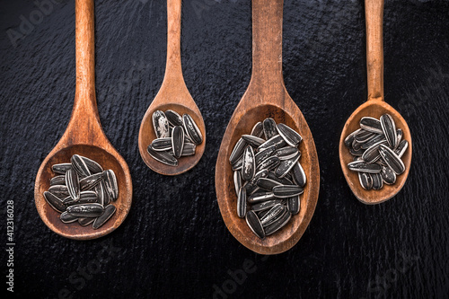 Sunflower seeds large overhead close-up arrangement in old wooden spoons on black shiny stone background studio shot