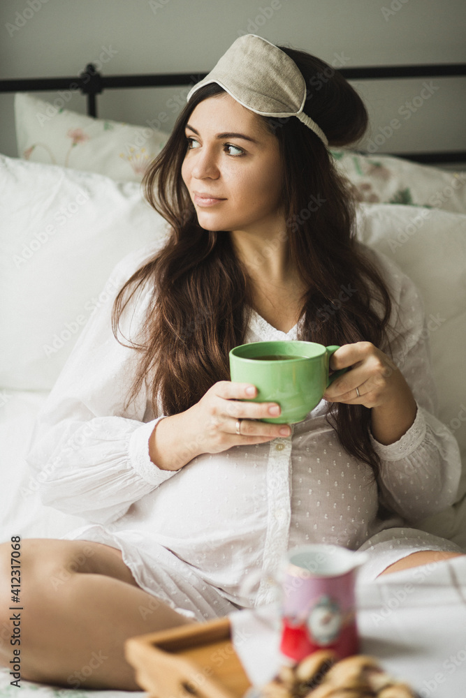 Pregnant woman with a cup sitting on a bed Pregnant woman with a cup sitting on a bed