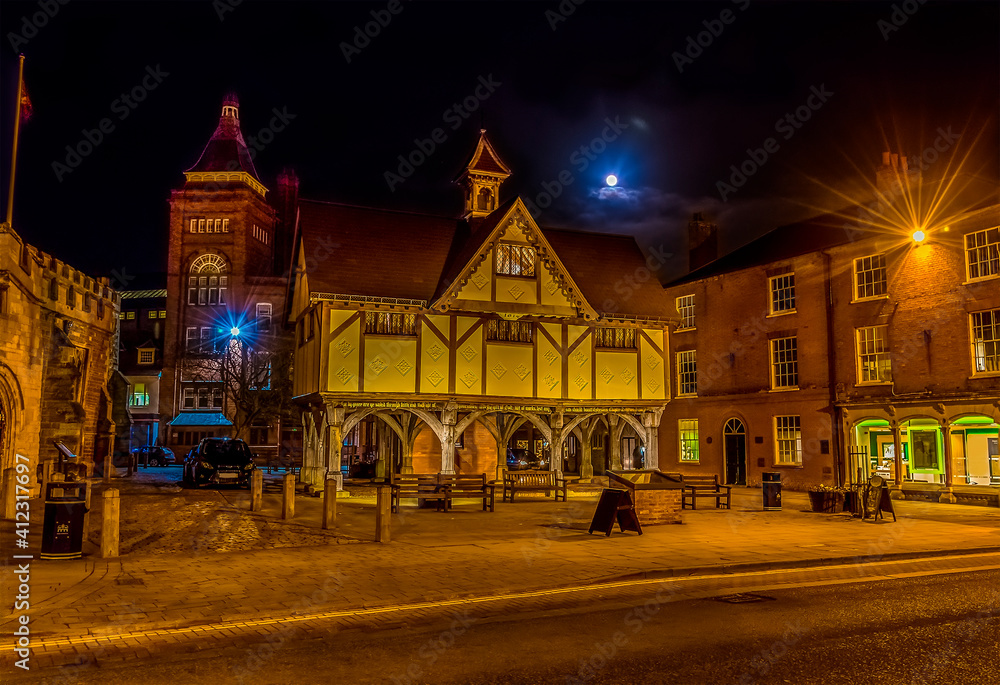 A view across the market square in Market Harborough, UK at night with a full moon in the background