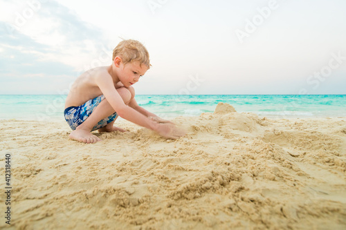 Boy Building Sand Castle on White Sand Tropical Beach WIth Turqu photo