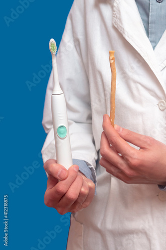 A guy in a white coat holds a white electric toothbrush and miswak (sivak), arak tree, Persian Salvador. Dental hygiene.