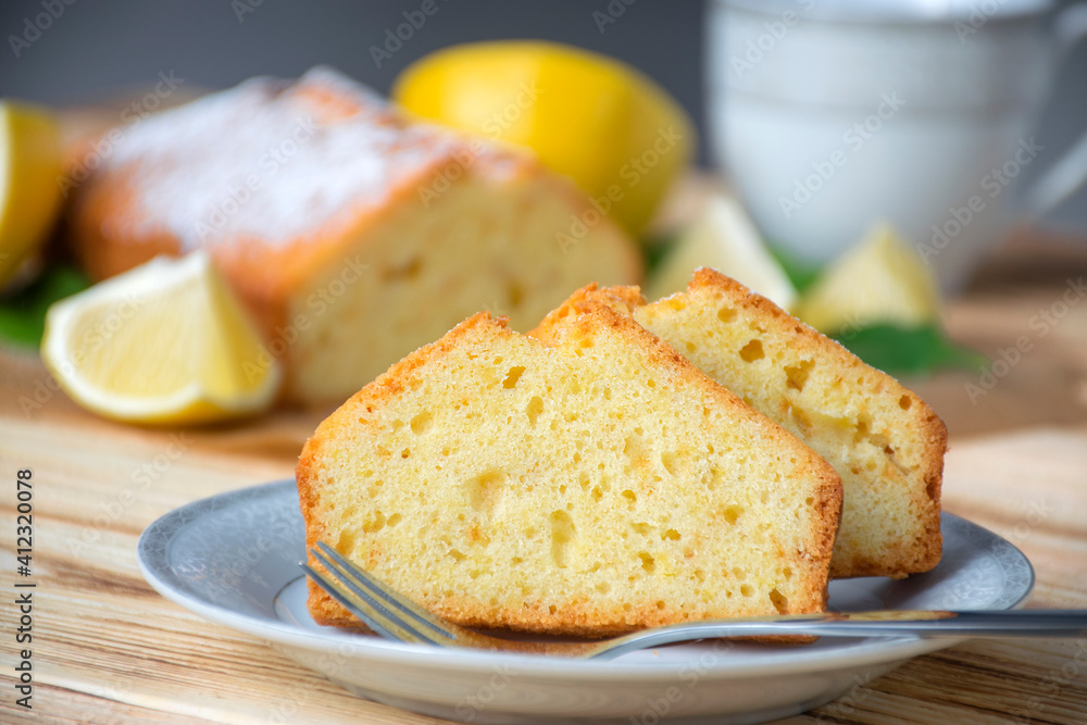 Piece of lemon cake on plate on rustic wooden board with full pie, lemons and cup on background. Easy recipe of citrus dessert for everyday cooking. Homemade bakery by classic recipe. Piece of lemon cake on plate on rustic wooden board with full pie, lemons and cup on background. Easy recipe of citrus dessert for everyday cooking. Homemade bakery by classic recipe.