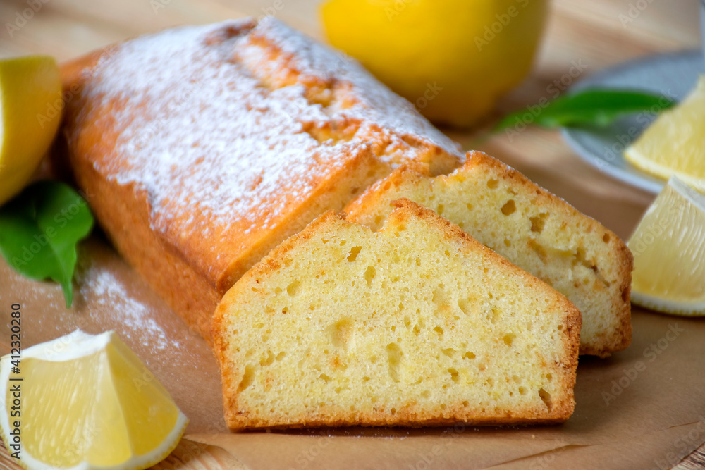 Loaf of gluten free lemon cake with sugar powder, pieces of lemon, green leaves on rustic wooden background. Close up slice of citrus pie by classic recipe. Healthy nutrition, homemade vegan dessert. Loaf of gluten free lemon cake with sugar powder, pieces of lemon, green leaves on rustic wooden background. Close up slice of citrus pie by classic recipe. Healthy nutrition, homemade vegan dessert.