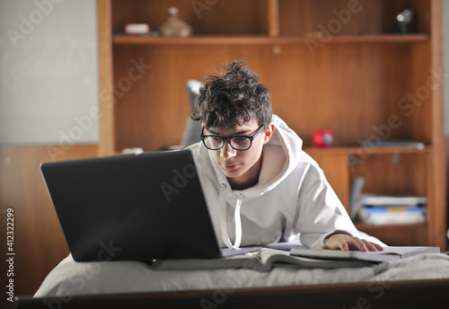 young boy studies on the bed with books and computer