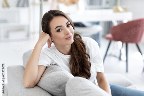 Beautiful smiling authentic woman look at camera, sitting on couch in living room at home.
