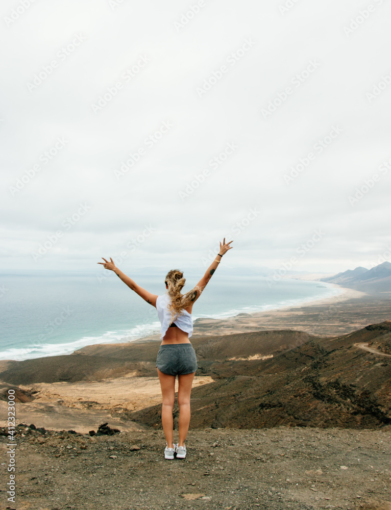 Woman raising arms with incredible landscape of mountains and beach Woman raising arms with incredible landscape of mountains and beach