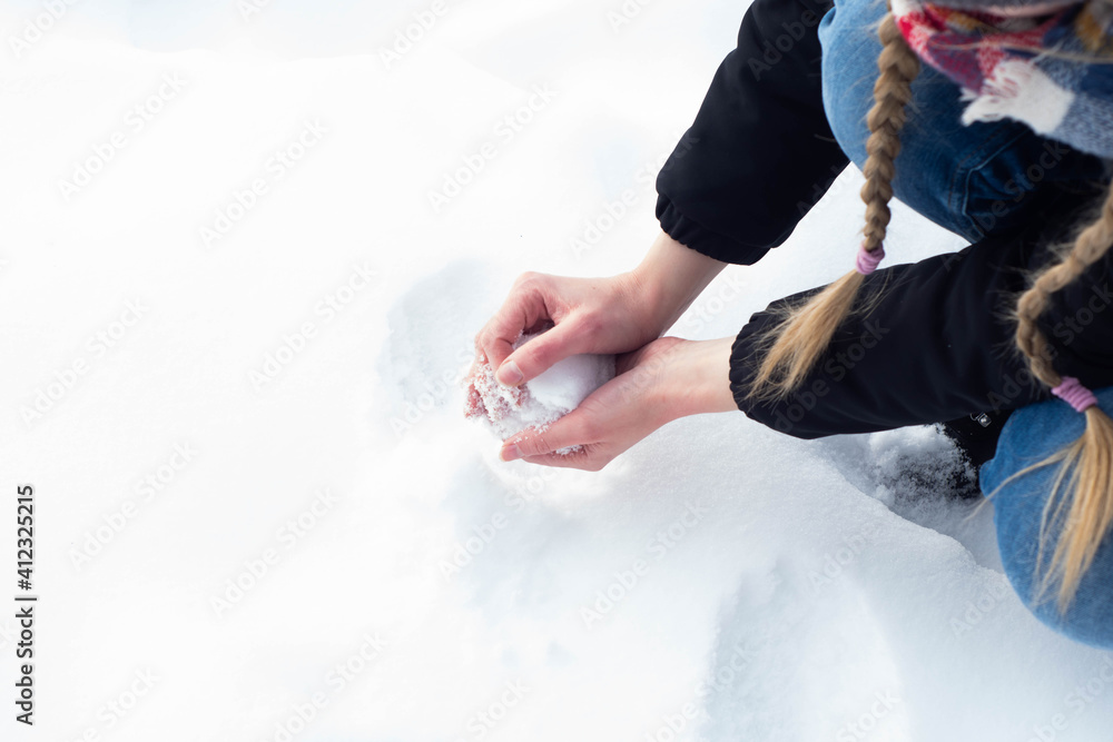 Girl in warm clothes playing on the snow during freezing cold winter. Forming a snow ball with bare hands, having winter fun.