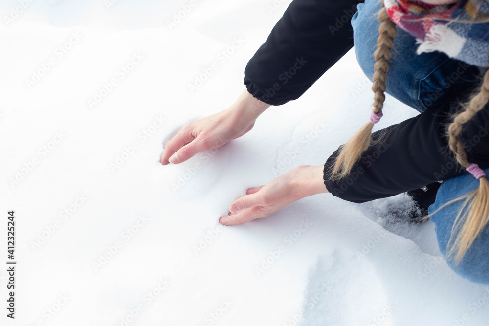 Girl in warm clothes playing on the snow during freezing cold winter. Forming a snow ball with bare hands, having winter fun.
