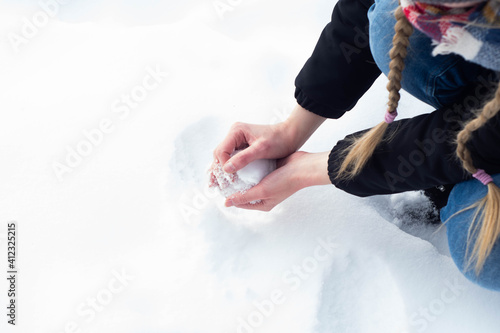 Obraz na płótnie Girl in warm clothes playing on the snow during freezing cold winter. Forming a snow ball with bare hands, having winter fun. w salonie