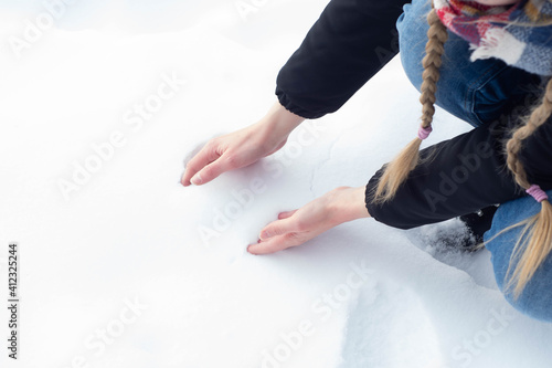 Girl in warm clothes playing on the snow during freezing cold winter. Forming a snow ball with bare hands, having winter fun.