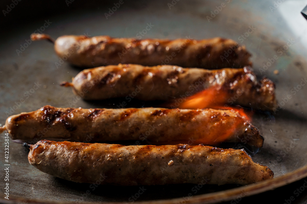 Fototapeta premium Grilled sausages in a frying pan are fired with a gas burner