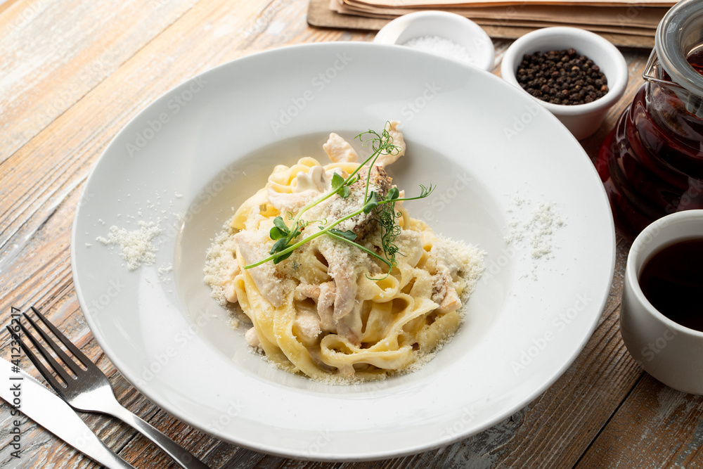 Chicken pasta with creamy sauce and grated parmesan cheese on a wide white plate Chicken pasta with creamy sauce and grated parmesan cheese on a wide white plate