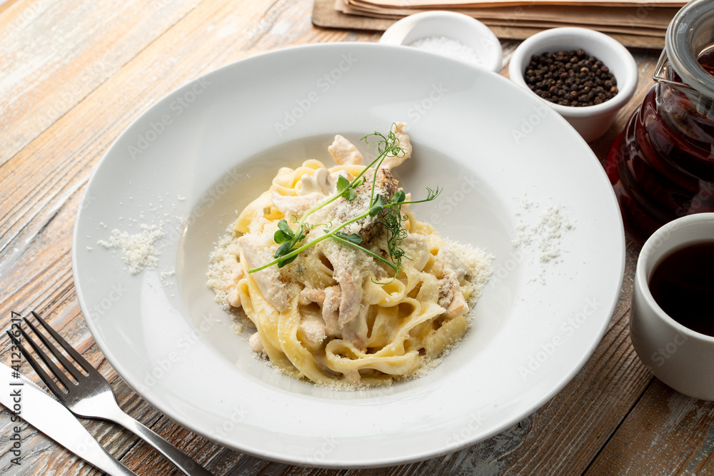 Chicken pasta with creamy sauce and grated parmesan cheese on a wide white plate