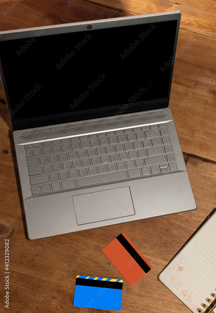 laptop with black screen orange credit cards and notepad on wooden table laptop with black screen orange credit cards and notepad on wooden table