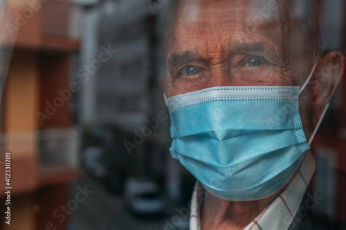 elderly man with face mask looking out the window in pandemic quarantine