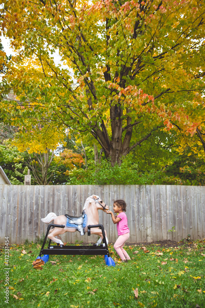 Portrait of a pretty happy young child playing with and feeding her rocking horse outdoors Portrait of a pretty happy young child playing with and feeding her rocking horse outdoors