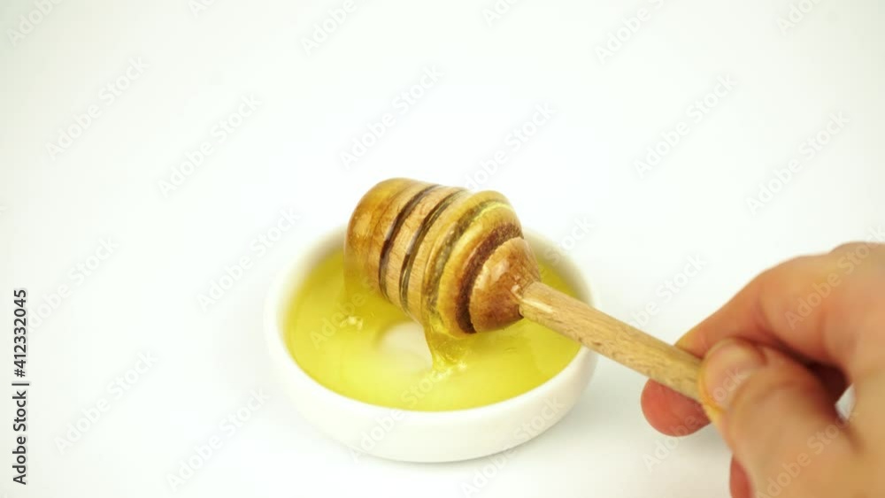 Liquid honey taking with wooden stick from small white plate Liquid honey taking with wooden stick from small white plate