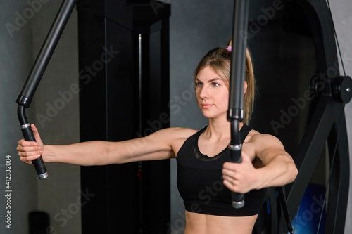 Sporty young blonde woman trains her arm muscles with the help of a simulator. Sports hall. Gym.