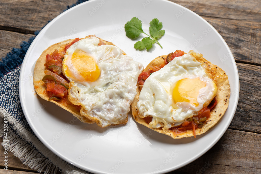 Fried eggs with sauce and tortilla called rancheros for breakfast on wooden background. Mexican food Fried eggs with sauce and tortilla called rancheros for breakfast on wooden background. Mexican food