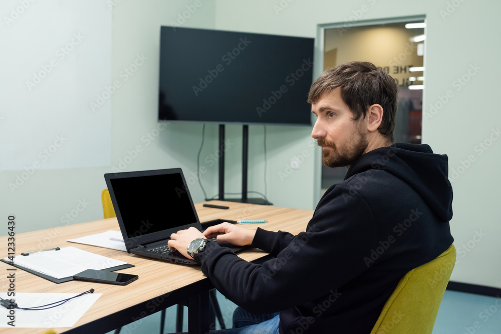Young man working on laptop sitting at his workplace in coworking office. Side view, business concept