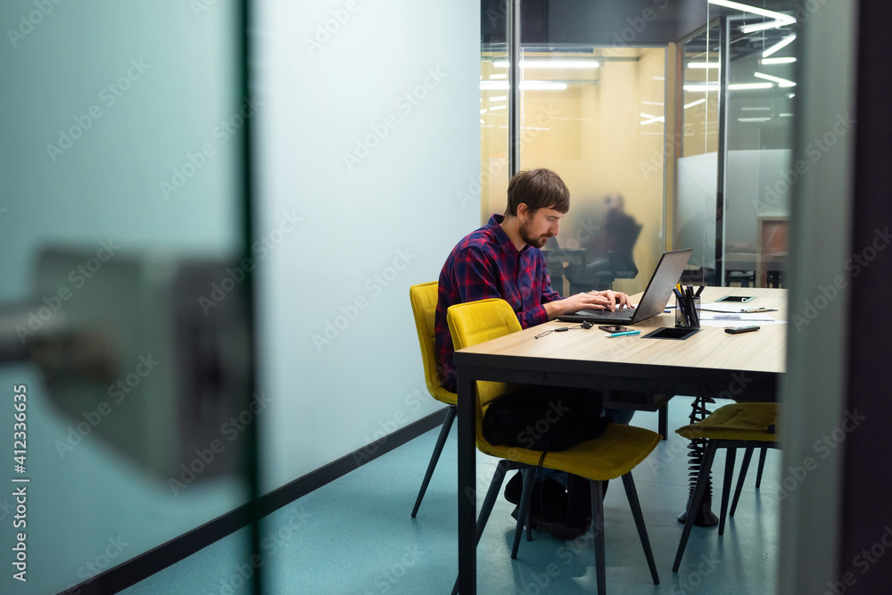 Young businessman working on a laptop sitting at his workplace in the office. Coworking, Startup, Business Concept Young businessman working on a laptop sitting at his workplace in the office. Coworking, Startup, Business Concept