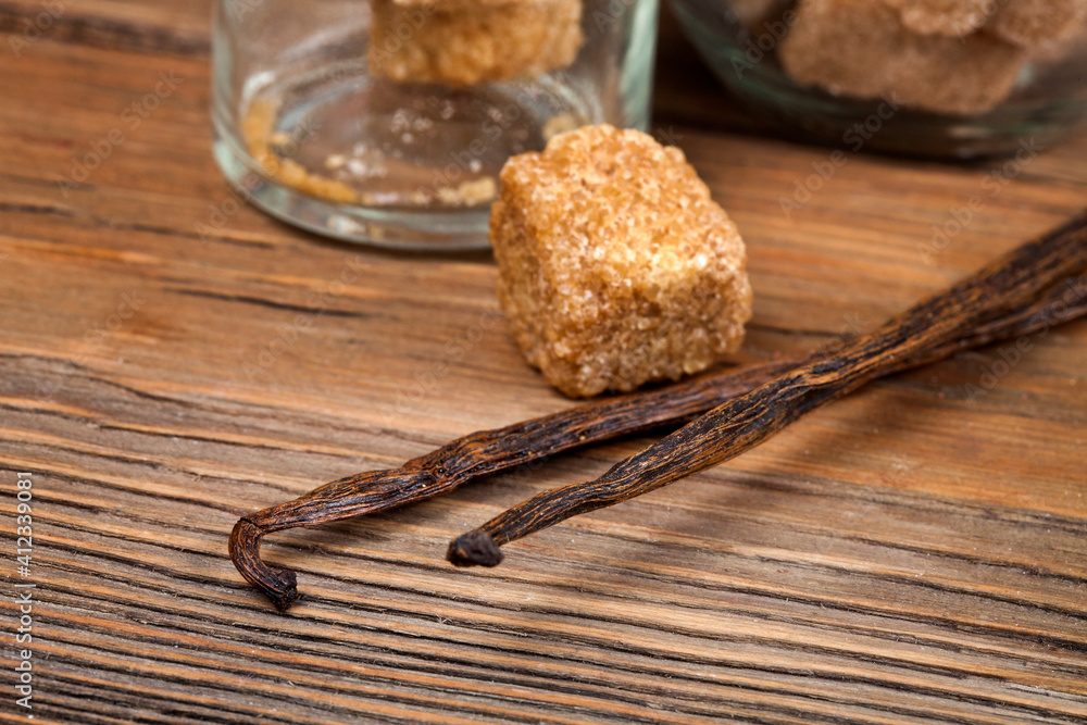 Fototapeta premium Vanilla beans with brown sugar pieces on a wooden background. Macro photography of spices.